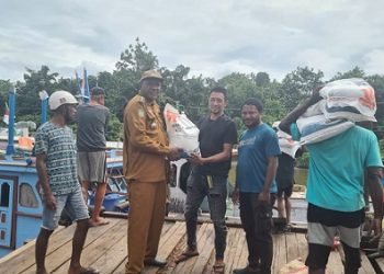 Koordinator lapangan (Korlap) Bulog dari Kantor Pos Cabang Mimika serahkan beras secara simbolis kepala Efraim Saria, Kadistrik Mimika Barat Jauh di Pomako yang selanjutnya oleh staf distrik serahkan kepada kepala kampung masing-masing untuk dibagikan kepada masyarakat. (Foto : Ist./Koranpapua.id)